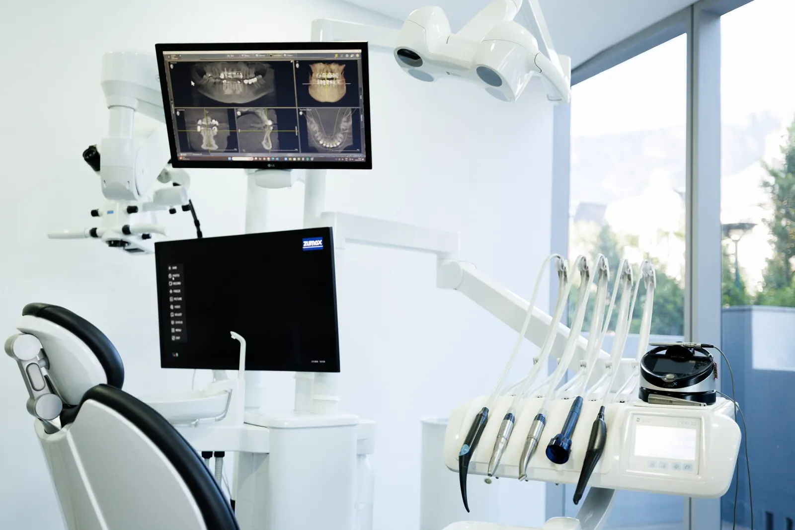 Treatment room with a dental microscope and a 3D X-ray on screen beside a large window
